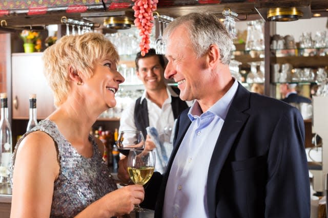 Senior couple in restaurant standing at bar with glass of wine in hand and having fun