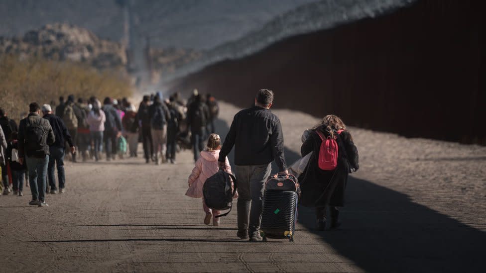 Asylum seeking migrants wait to be processed by the US Border Patrol after crossing from Mexico at a makeshift camp next to the US border wall on December 13, 2023 in Jacumba Hot Springs, California