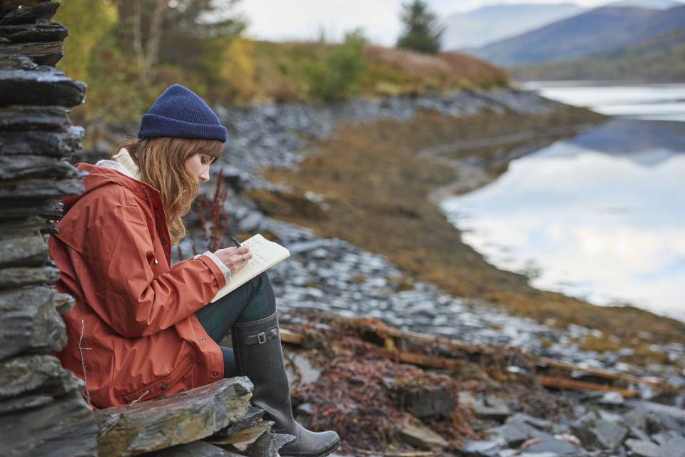 A girl writing in a journal by the river