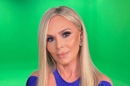 Tamra sitting in front of a green screen in a blue jumpsuit.