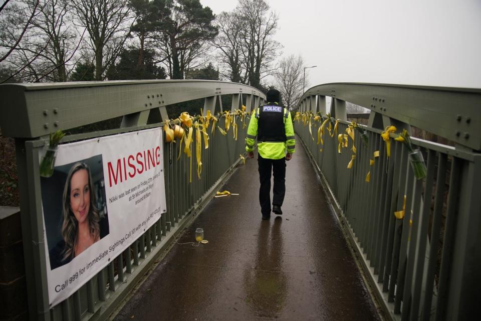 A police officer walks past a missing person appeal poster for Nicola Bulley and yellow ribbons and messages of hope tied to a bridge over the River Wyre (Peter Byrne/PA)