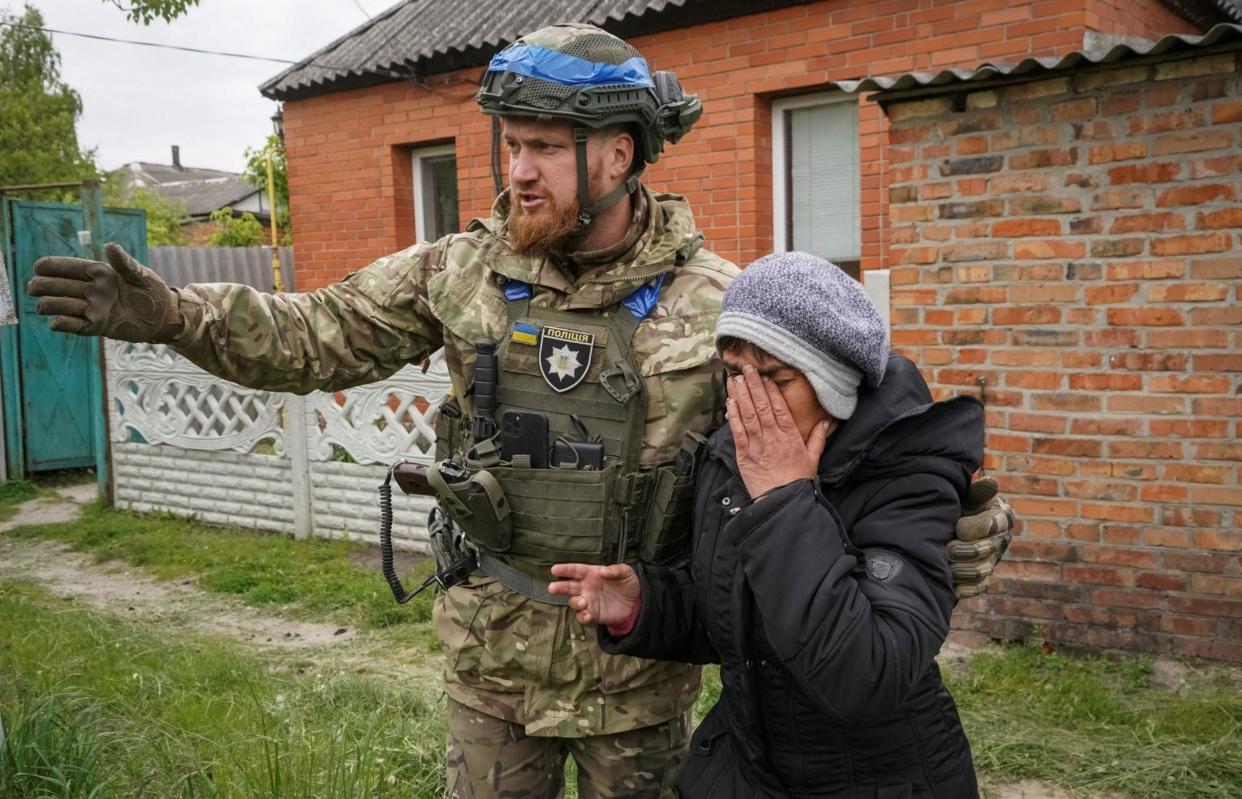 Ukrainian soldier in uniform helping a woman in tears evacuate from village in Kharkiv