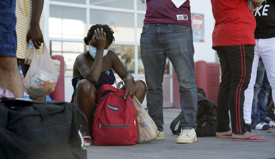 Migrants, mostly from Haiti, wait for a bus after they were processed and released after spending time at a makeshift camp near the International Bridge, Sunday, Sept. 19, 2021, in Del Rio, Texas. The U.S. flew Haitians camped in the Texas border town back to their homeland Sunday and tried blocking others from crossing the border from Mexico in a massive show of force that signaled the beginning of what could be one of America's swiftest, large-scale expulsions of migrants or refugees in decades. (AP Photo/Eric Gay)