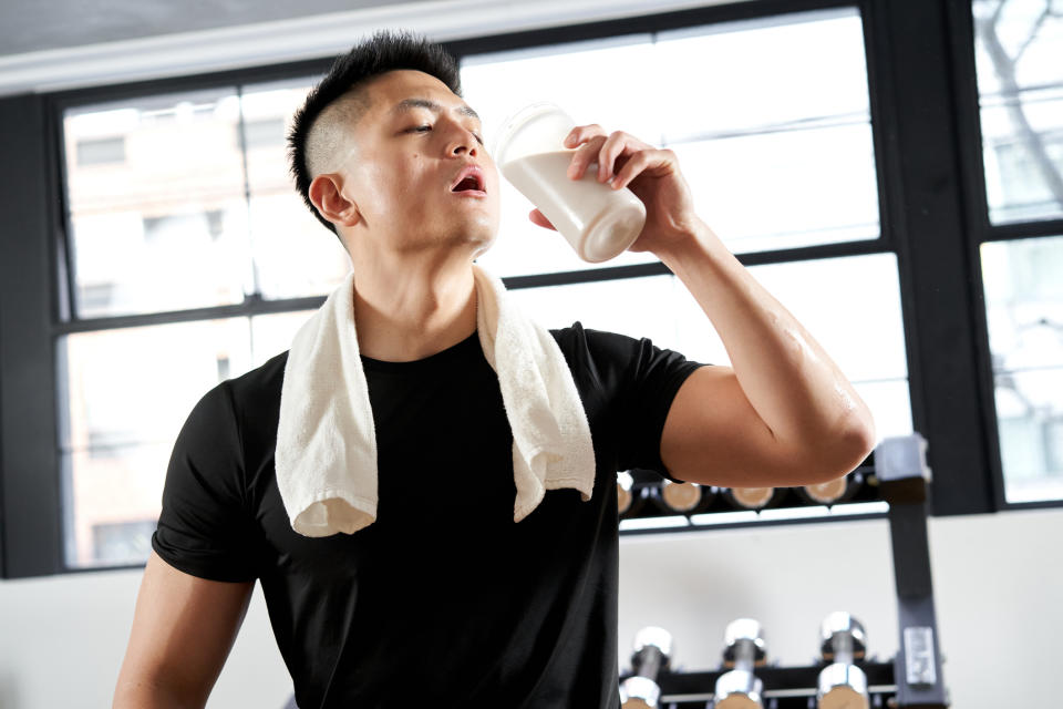 Person in gym attire with towel around neck drinking from a cup