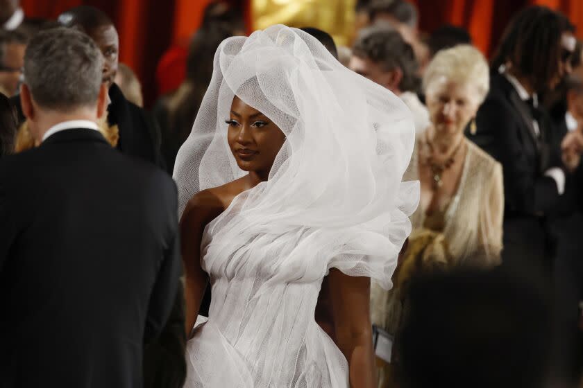 A woman mingles at an awards ceremony in a structural white gown with a feature that goes all around her head