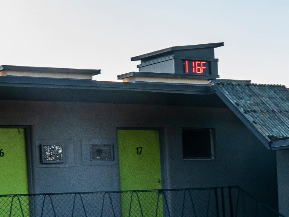 A person stands in front of a building where the temperature reads 116 degrees Fahrenheit.