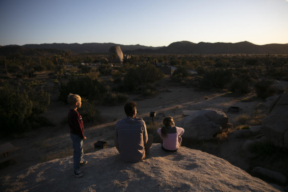 FILE - In this May 19, 2020, file photo Aaron Stubbs and his two children sit on a rock to watch sunset at Joshua Tree National Park in California. The Biden administration is outlining a plan to sharply increase conservation of public lands and waters over the next decade. A report to be issued Thursday recommends a series of steps to achieve a nationwide goal to conserve 30% of U.S. lands and waters by 2030. (AP Photo/Jae C. Hong, File)