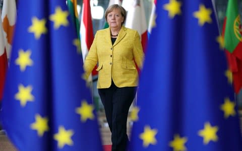 German Chancellor Angela Merkel walks into an EU summit at the Europa building in Brussels through different nations' flags with the EU flag on both her left and right hand side, on Thursday, Dec. 14, 2017, wearing a yellow suit jacket and black trousers - Credit: Oliver Matthys/AP