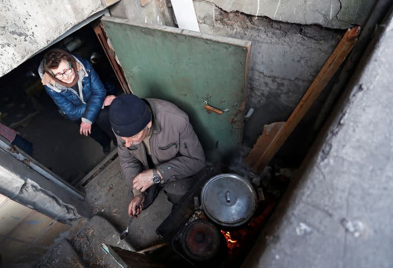 Local residents cook food at the entrance to the basement of an apartment building in Mariupol