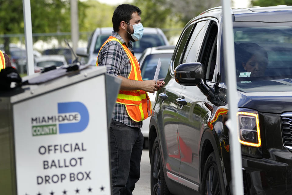 FILE - In this Monday, Oct. 26, 2020, file photo, an election worker takes ballots from voters dropping them off at an official ballot drop box at the Miami-Dade County Board of Elections, in Doral, Fla. Just days before the presidential election, millions of mail-in ballots have still not been returned in key battleground states. Many of those are due in county offices by Tuesday, Nov. 3, but the latest Postal Service delivery data suggests it’s too late for voters to drop their ballots in the mail. (AP Photo/Lynne Sladky)