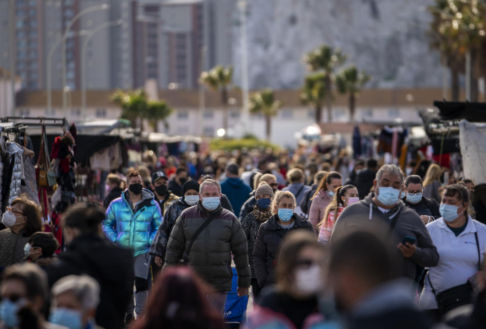 FILE - In this Jan. 4, 2021, file photo, people wearing face masks walk along the stalls of a weekly market in the Spanish city of La Linea. While most of Europe kicked off 2021 with earlier curfews or stay-at-home orders, authorities in Spain insist the new coronavirus variant wreaking havoc elsewhere is not to blame for a sharp resurgence of cases and that the country can avoid a full lockdown even as its hospitals fill up. (AP Photo/Emilio Morenatti, File)