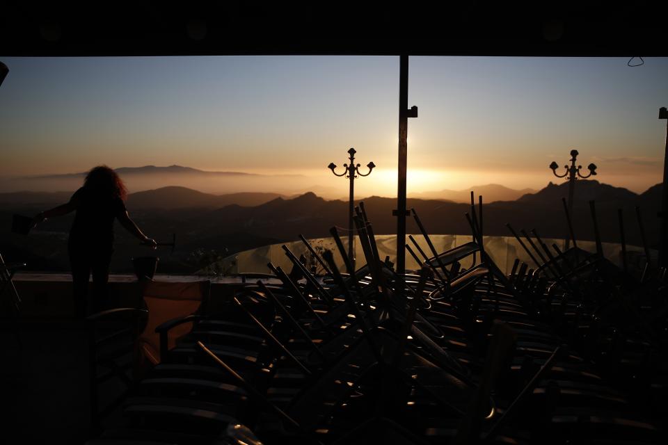 A woman cleans the garden of an all-day cafe bar restaurant as the sun sets in Apeiranthos village, on the Aegean island of Naxos, Greece, Tuesday, May 11, 2021. With debts piling up, southern European countries are racing to reopen their tourism services despite delays in rolling out a planned EU-wide travel pass. Greece Friday became the latest country to open up its vacation season as it dismantles lockdown restrictions and focuses its vaccination program on the islands. (AP Photo/Thanassis Stavrakis)