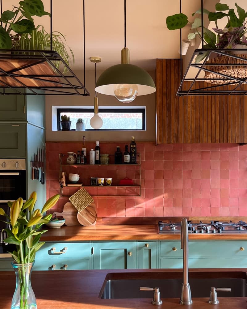 Pink tile backsplash in kitchen with green cabinets.