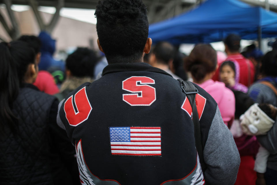 A man in a "USA" jacket waits with migrants at the El Chaparral border crossing to hear names called out on Nov. 28. (Photo: Mario Tama via Getty Images)