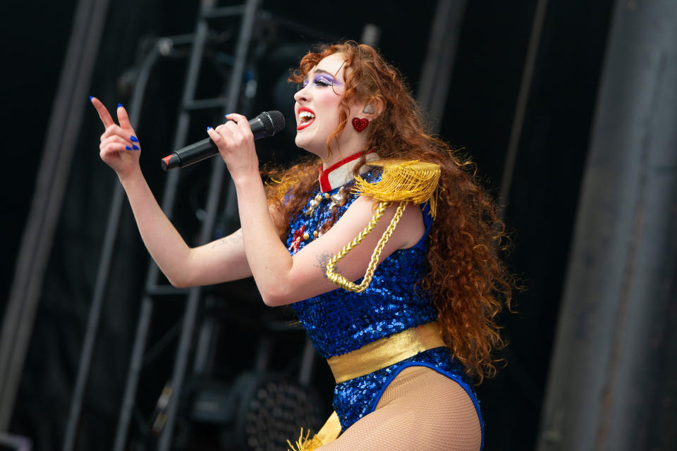 Music artist Chappell Roan, performs energetically on stage wearing a sequined outfit with shoulder embellishments, holding a microphone