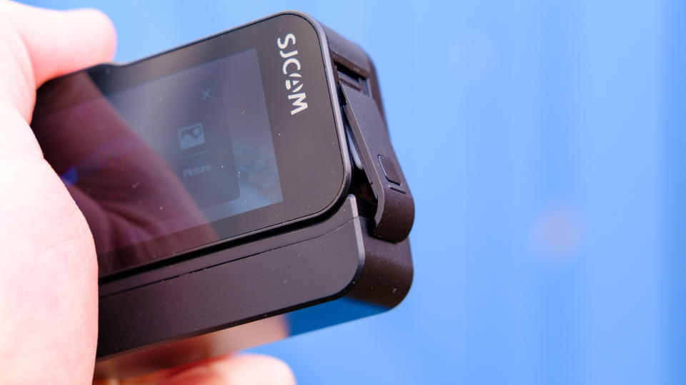 A photo of the SJCAM Sj20 being held up with the USB-C and cart port showing against a blue backdrop.