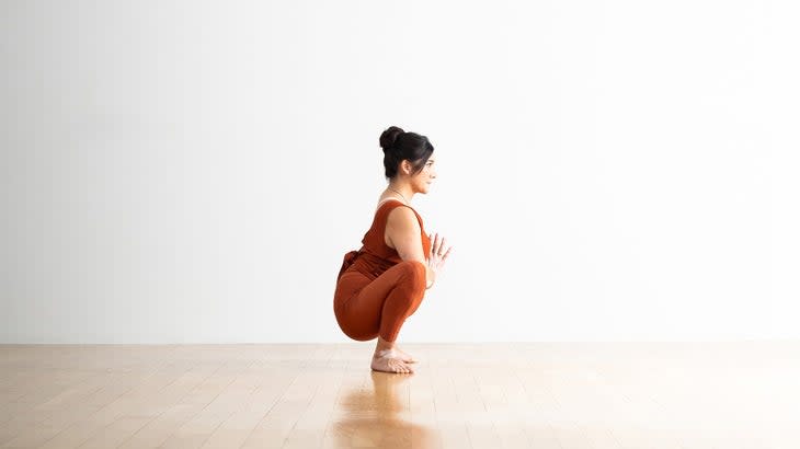 A person demonstrates a Squat or Garland Pose in yoga