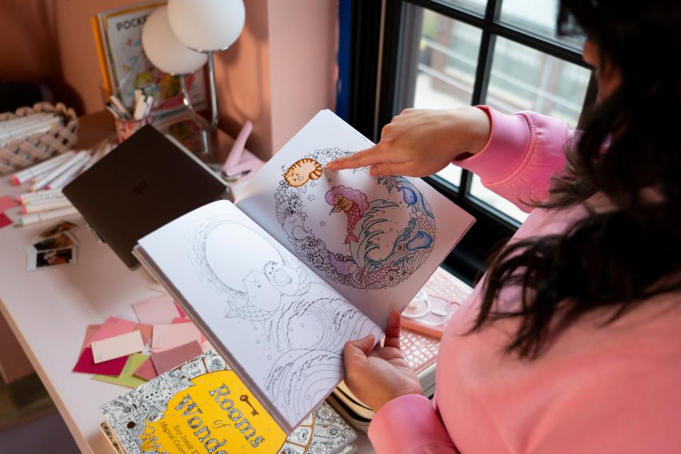 Kelly Marcelo, a local content creator, flips through one of her coloring books, Friday, March 1, 2024, in her apartment in Indianapolis. Marcelo curates in a style she describes as hyper-feminine, “refined maximalism.” She finds most of furniture and decorations on Facebook Marketplace or while thrifting.