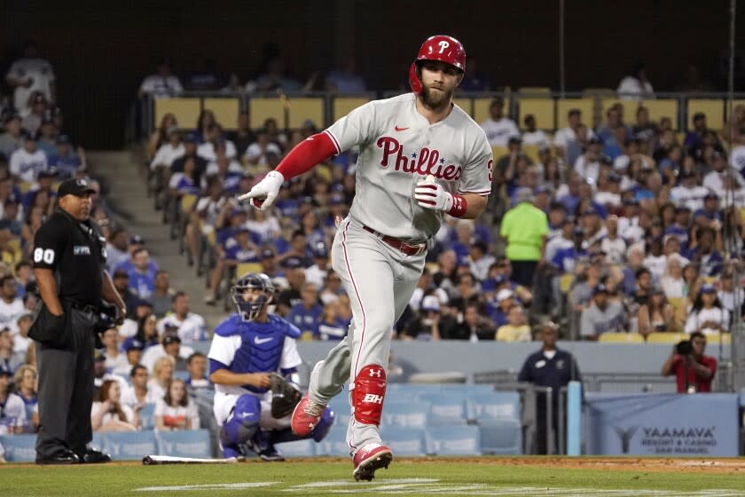 Philadelphia Phillies' Bryce Harper, right, gestures toward his dugout as he heads to first.