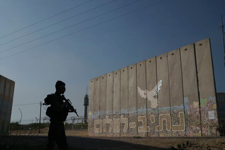 Un soldado israelí junto a un muro de seguridad con la frase 