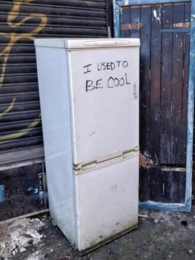 An old, dirty refrigerator is standing outside with the graffiti text "I used to be cool" written on its door