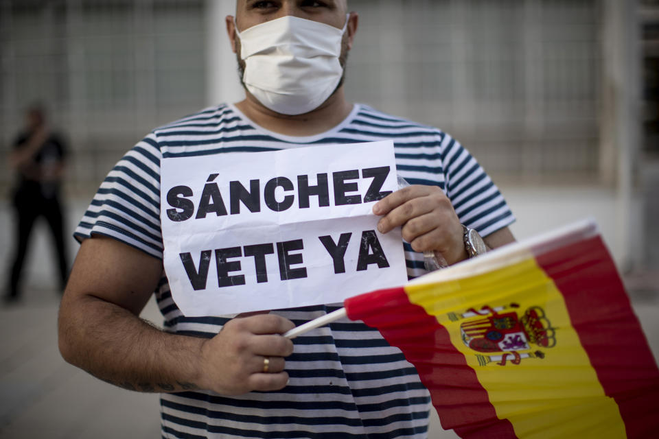 A man holds a Spanish flag and banner reading in Spanish: "Sanchez go away" during a protest against the Spanish government amid the lockdown to prevent the spread of coronavirus in Alcorcon, Spain, Friday, May 22, 2020. The Spanish government is allowing Madrid and Barcelona to ease their lockdown measures, which were introduced to fight the coronavirus pandemic. (AP Photo/Manu Fernandez)