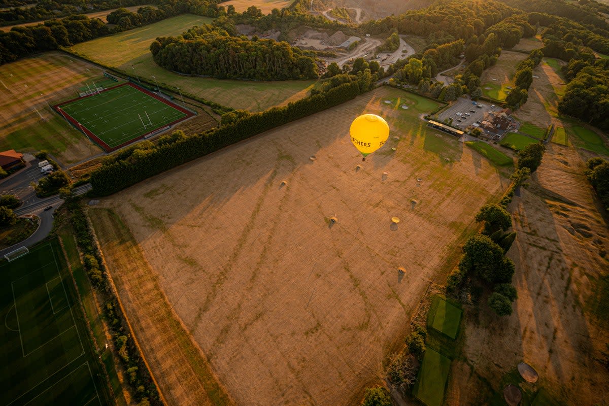 A hot air balloon flies over a browning and parched golf driving range in Somerset (Ben Birchall/PA) (PA Wire)