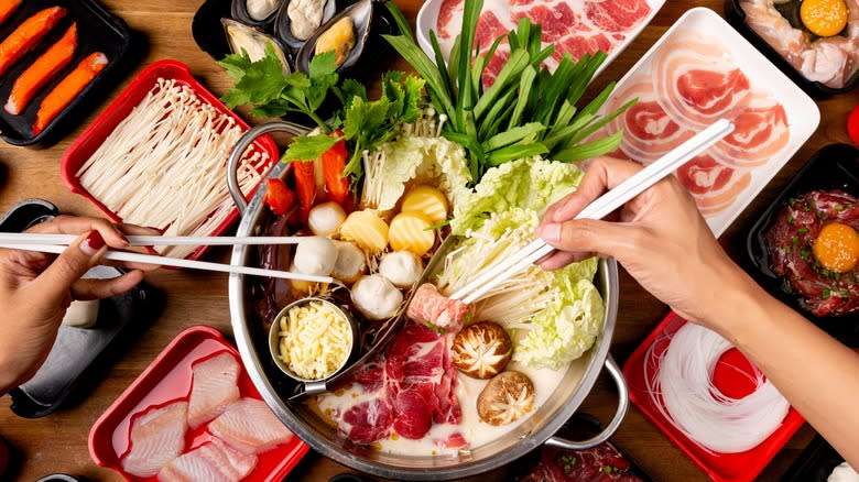 Hands adding food to shabu-shabu