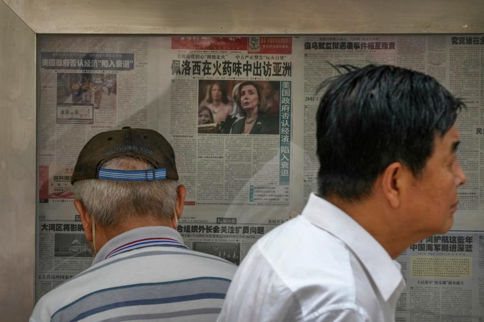 A resident walks by a man reads a newspaper reporting on U.S. House Speaker Nancy Pelosi's Asia visit, at a stand in Beijing, Sunday, July 31, 2022.