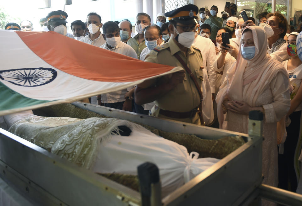 A police officer places an Indian national flag over the coffin of Bollywood icon Dilip Kumar during his funeral in Mumbai, India, Wednesday, July 7, 2021. Dilip Kumar, hailed as the "Tragedy King" and one of Hindi cinema's greatest actors, died Wednesday in a Mumbai hospital after a prolonged illness. He was 98. (Kunal Patil/Pool photo via AP)