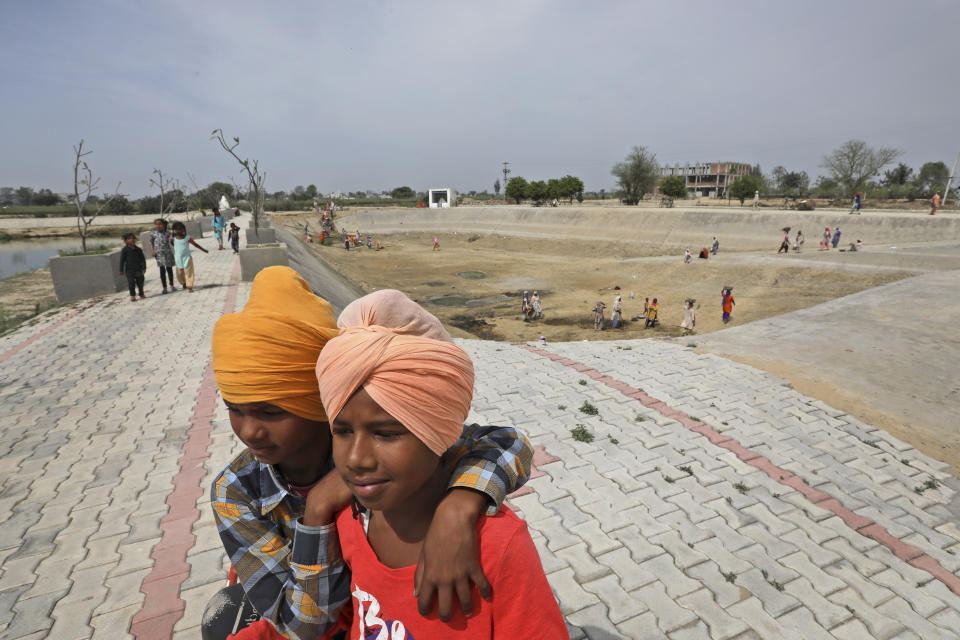 Children play as villagers clean a sewage treatment in Ranish Kalan village in Moga district of Indian state of Punjab, Saturday, March 13, 2021. The residents of Ransih Kalan village, have begun taking steps to conserve water. Villagers have installed a sewage treatment plant, and the treated water is then used for irrigation. They've also set up plants to harvest rainwater, which is then diverted into a man-made lake. (AP Photo/Manish Swarup)