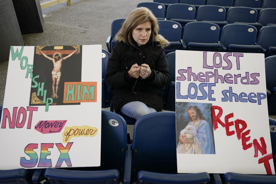 FILE - A woman sits with signs while praying the Rosary with a group during a rally outside of the Baltimore hotel where the United States Conference of Catholic Bishops are holding its Fall General Assembly meeting in Baltimore, Nov. 16, 2021. The city of Baltimore has agreed to pay $275,000 toward the legal fees of a far-right Catholic media group to settle a lawsuit over the city's unsuccessful attempt to block a rally in 2021. (AP Photo/Julio Cortez, File)