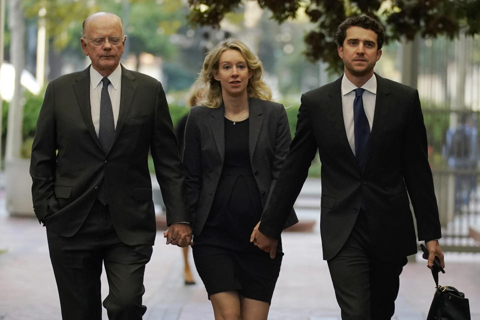 File - Former Theranos CEO Elizabeth Holmes, center, arrives at federal court with her father, Christian Holmes IV, left, and partner, Billy Evans, in San Jose, Calif., Monday, Oct. 17, 2022. As Elizabeth Holmes prepares to report to prison next week, the criminal case that laid bare the blood-testing scam at the heart of her Theranos startup is entering its final phase. (AP Photo/Jeff Chiu, File)
