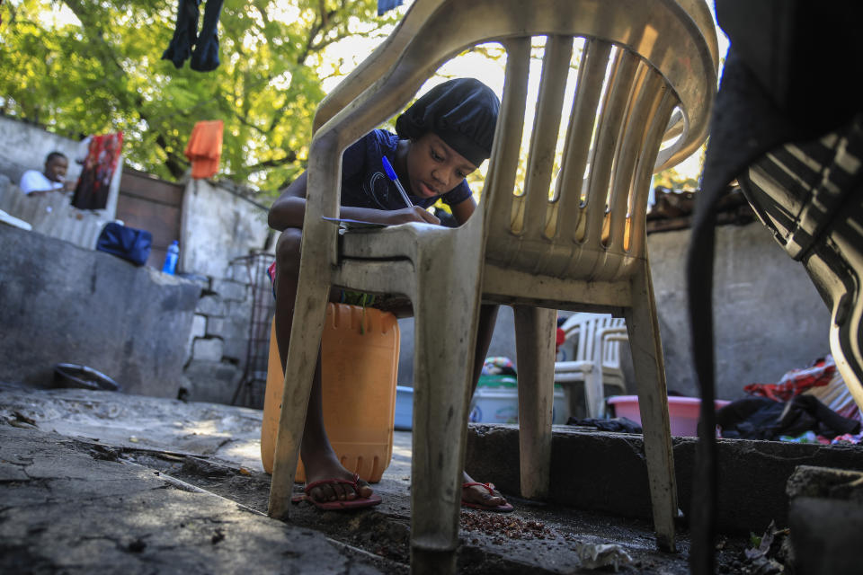 Christina Julien does her homework on a chair in Port-au-Prince, Haiti, Sunday, Jan. 22, 2023. Julien is one of the thousands of people in the capital who has been forced to flee her home due t violence, seeking refuge with family members in another part of the city. (AP Photo/Odelyn Joseph)