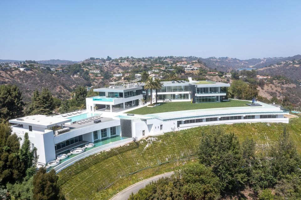 an aerial view of a white mansion, The One Bel Air, and its pools, surrounded by hills and green grass