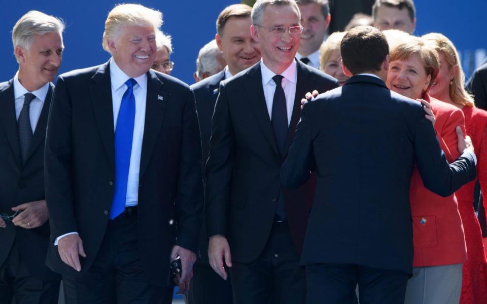 Mr Macron greets Mrs Merkel before shaking hands with Mr Trump at the summit - Credit: AFP