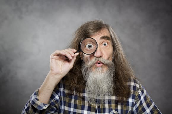 A man with a beard holding a magnifying glass to his eye.