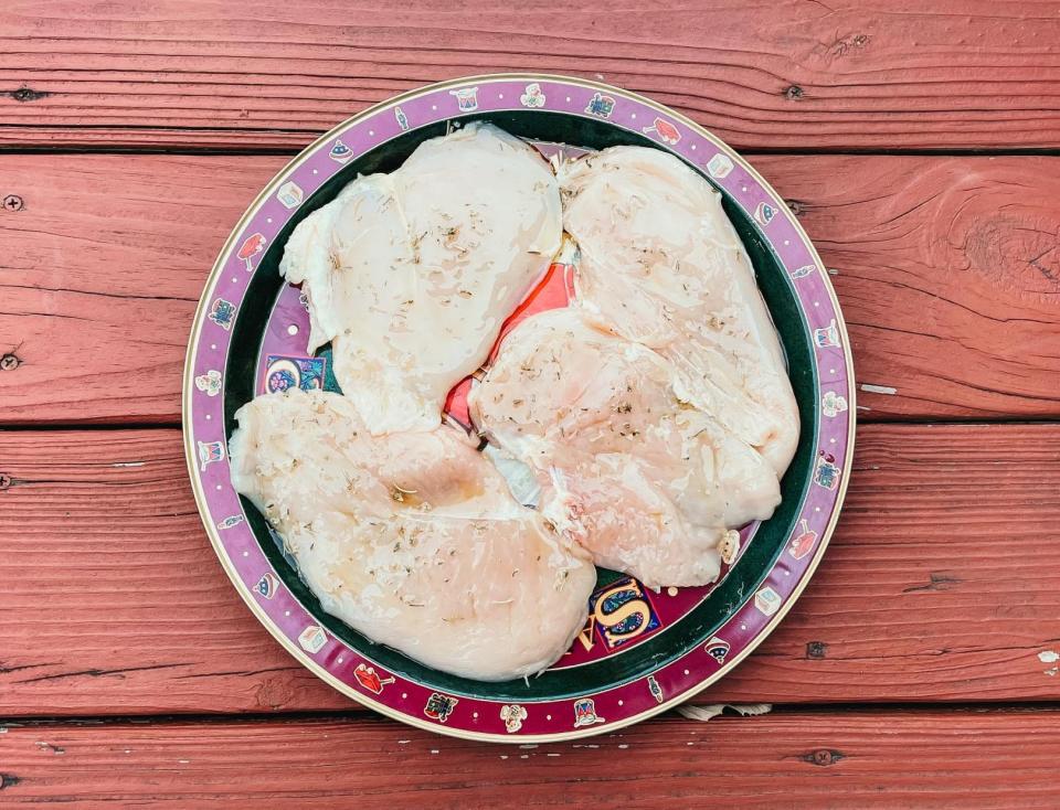 four pieces of raw chicken sitting on a kitchen plate
