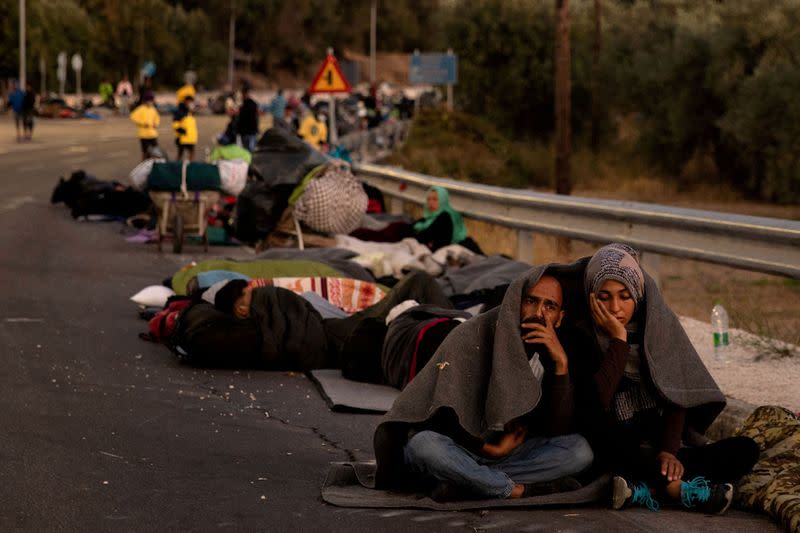 FILE PHOTO: Couple sits covered with a blanket as refugees and migrants camp on a road following a fire at the Moria camp on the island of Lesbos