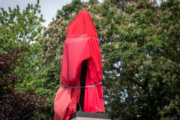 The statue of former Canadian prime minister Sir John A. Macdonald is covered by a red sheet in Kingston, Ont. on June 11, 2021. Local indigenous groups want the statue removed but the City of Kingston has not decided what to do with it. (Lars Hagberg/The Canadian Press - image credit)