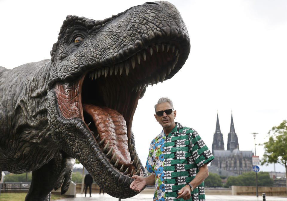 El actor Jeff Goldblum frene a una figura de dinosaurio T-Rex con la catedral de Colonia en el fondo durante una sesión de la película Jurassic World Dominion, en Colonia, alemania el 29 de mayo de 2022. (Thomas Banneyer/dpa via AP)