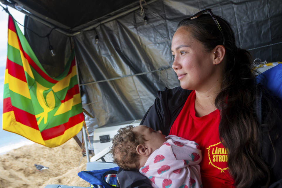 Jordan Ruidas sits with her daughter, Friday, Dec. 1, 2023, in Lahaina, Hawaii. Lahaina Strong has set up a "Fish-in" to protest living accommodations for those displaced by the Aug. 8, 2023 wildfire, the deadliest U.S. wildfire in more than a century. More than four months after the fire, tensions are growing between those who want to welcome tourists back to provide jobs and those who feel the town isn't ready for a return to tourism." (AP Photo/Ty O'Neil)