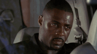 Idris Elba in the backseat of a car, scoffing