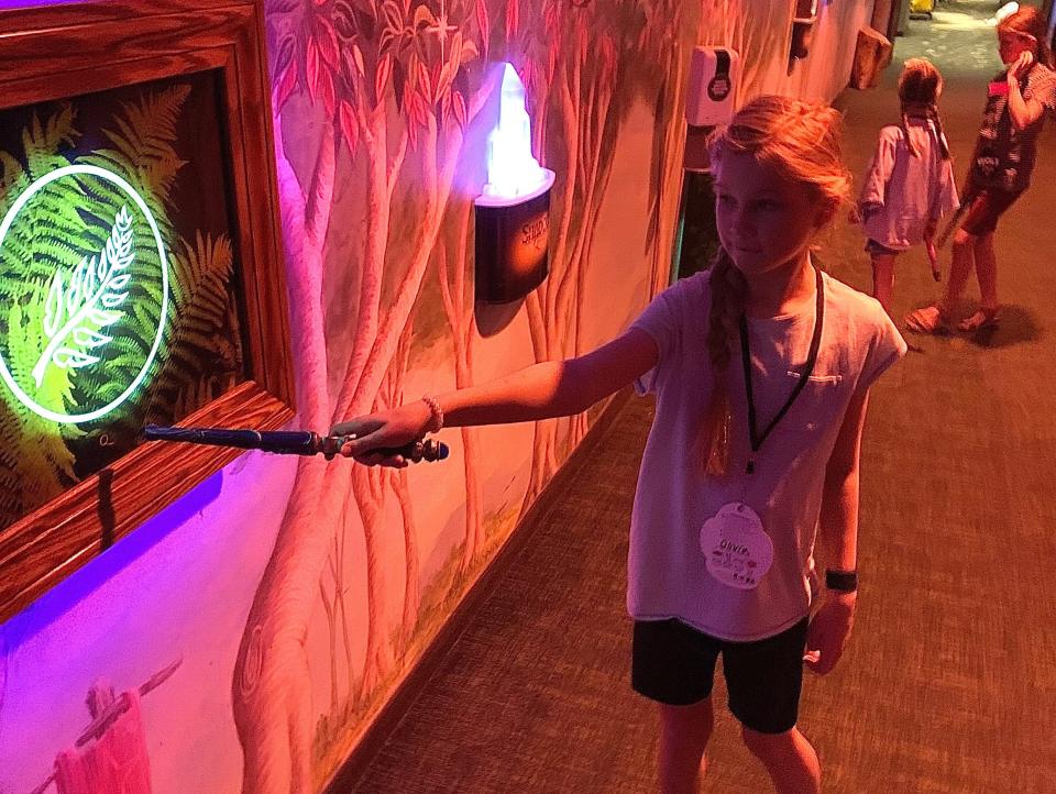 A girl pointing a wand at a lit up sign with a leaf on it.