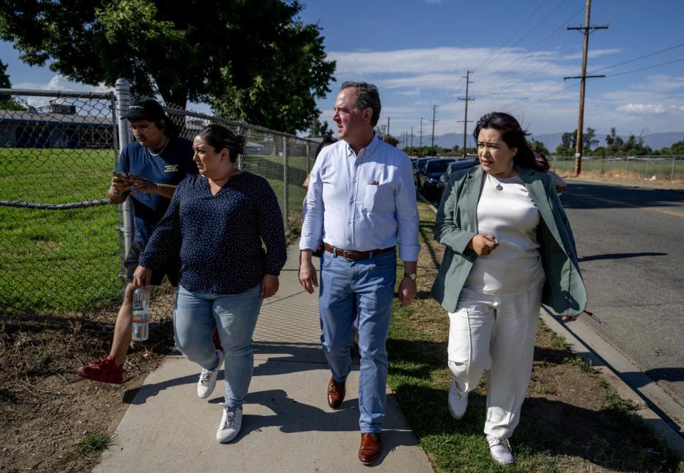 Congressman Adam Schiff, in jeans and a long-sleeved shirt, walks by a field with other people next to him