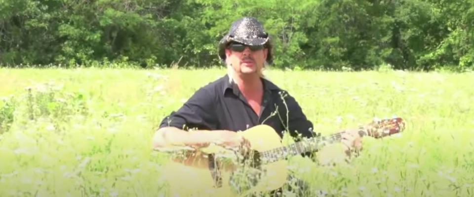 Joe Exotic playing a guitar in a field