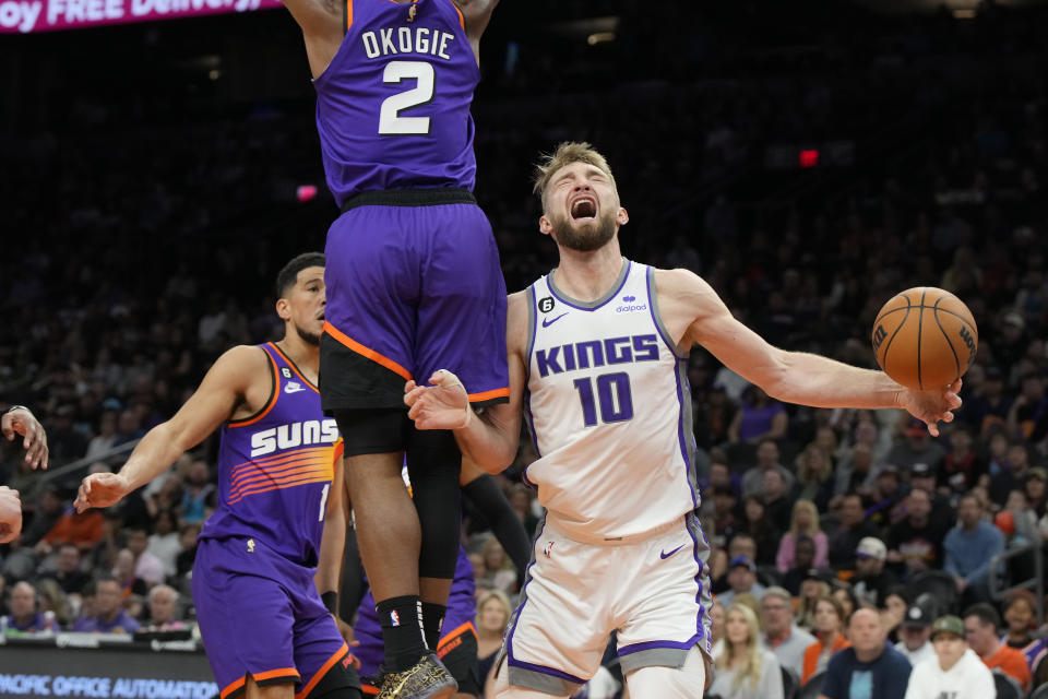 Sacramento Kings forward Domantas Sabonis (10) reacts after driving between Phoenix Suns guard Devin Booker and forward Josh Okogie (2) during the first half of an NBA basketball game, Saturday, March 11, 2023, in Phoenix. (AP Photo/Rick Scuteri)