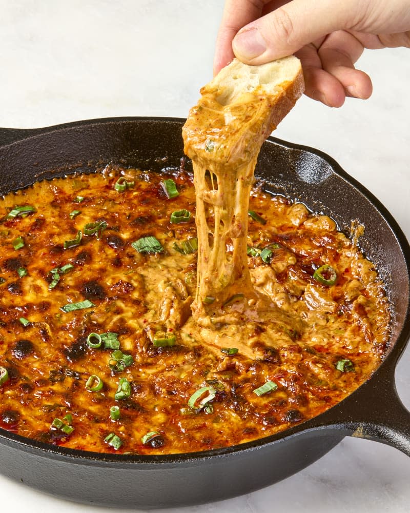 overhead shot of a baguette being dipped into the cheesy kimchi dip.