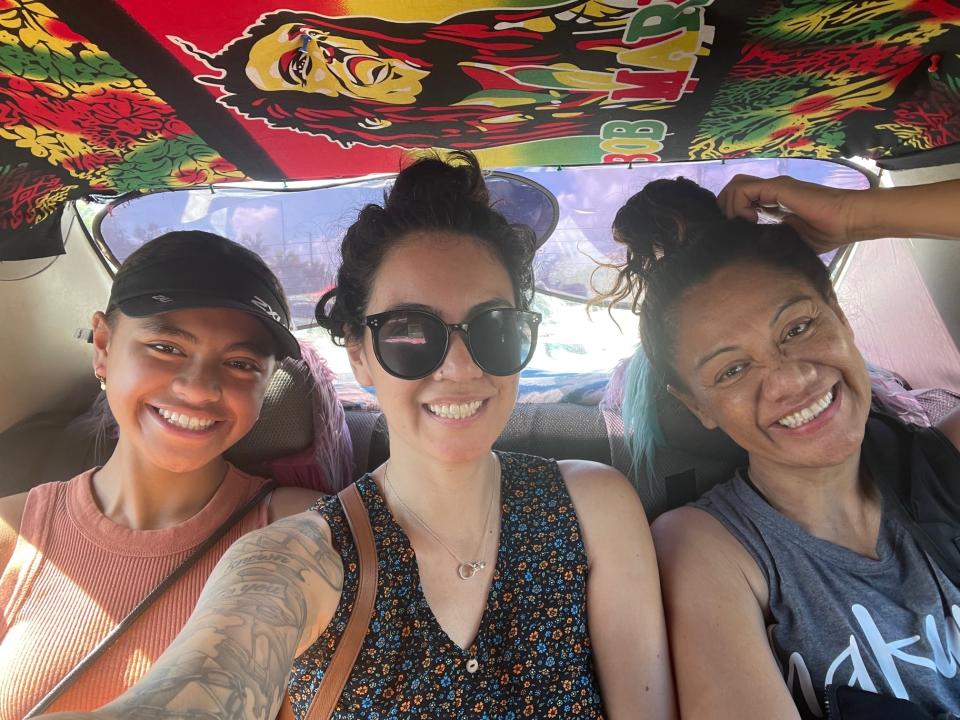 Three smiling women in the back of a car with a Bob Marley–themed interior roof