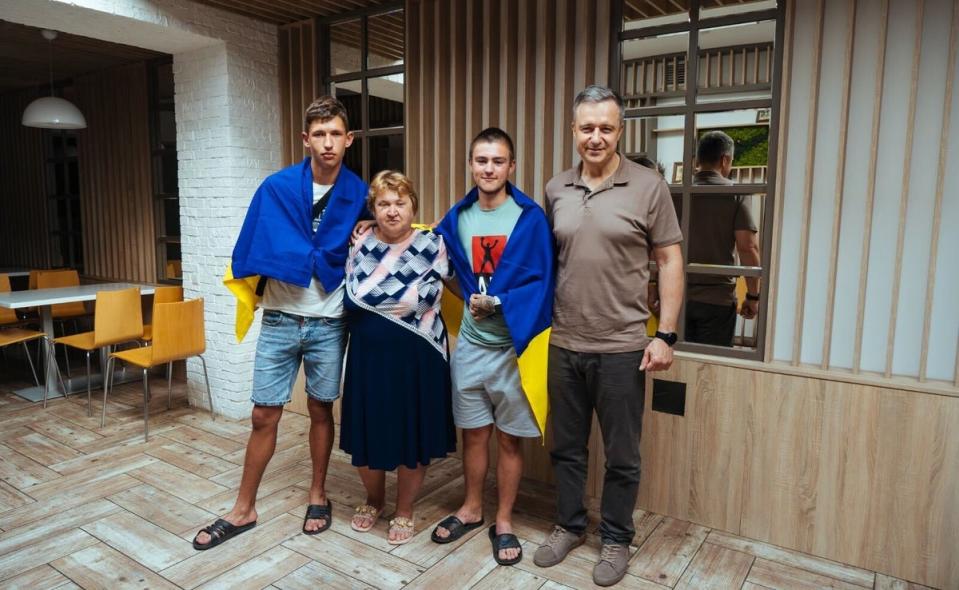 Teenagers Serhiy (left) and Denis Berezhnyi (centre right) stand at the Save Ukraine HQ in Kyiv with Mykola Kuleba (right) after being rescued from occupied Crimea in June 2023. Ukrainian flags are draped over their shoulders, as is custom for all children upon their return home (Save Ukraine)
